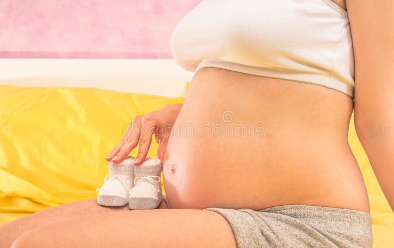 Schwangere Frau, die Babybeutenschuhe hält