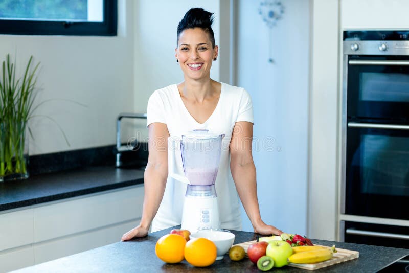 Pregnant woman smiling while standing in kitchen with blender and fruits on worktop. Pregnant woman smiling while standing in kitchen with blender and fruits on worktop