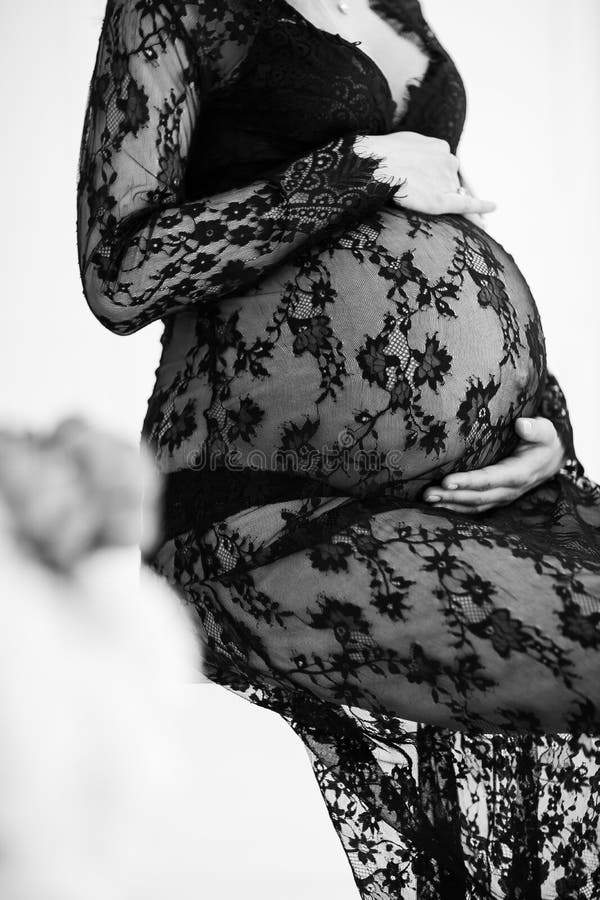Schwangere Frau im schwarzen Kleid hält Hände auf Bauch auf einem weißen Hintergrund lizenzfreies stockfoto Schwangere Frau im schwarzen Kleid hält Hände auf Bauch auf einem weißen Hintergrund lizenzfreies stockfoto