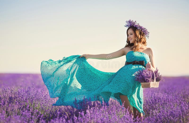 Happy pregnant brunette woman with long curly hair,large belly,dressed in a long dress turquoise,a hand holding a basket of flowers ,on her head is a wreath of field of lavender,picking flowers on a summer meadow mountain lavender. Happy pregnant brunette woman with long curly hair,large belly,dressed in a long dress turquoise,a hand holding a basket of flowers ,on her head is a wreath of field of lavender,picking flowers on a summer meadow mountain lavender