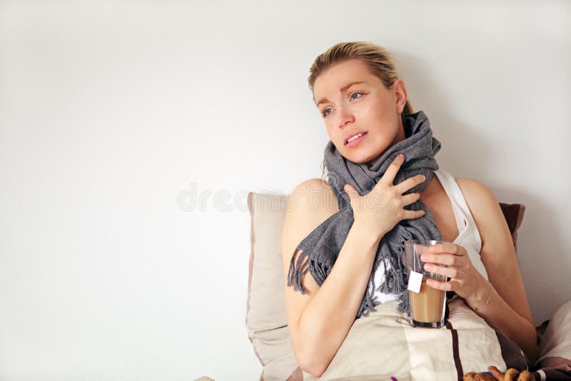Beautiful pregnant woman with a pained expression sitting up against a pillow clutching a scarf around her neck suffering with seasonal flu. Beautiful pregnant woman with a pained expression sitting up against a pillow clutching a scarf around her neck suffering with seasonal flu
