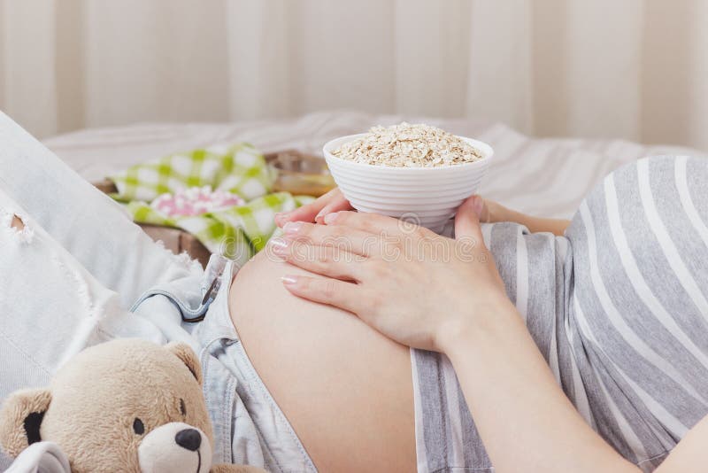 Schwangere Frau mit einer Schüssel des Hafermehls auf dem Bauch stockfotografie Schwangere Frau mit einer Schüssel des Hafermehls auf dem Bauch stockfotografie