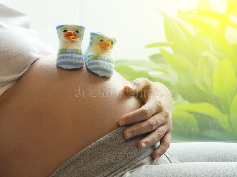 Schwangere Frau mit kleinen Schuhen für das ungeborene Baby auf dem Bauch lizenzfreies stockbild Schwangere Frau mit kleinen Schuhen für das ungeborene Baby auf dem Bauch lizenzfreies stockbild