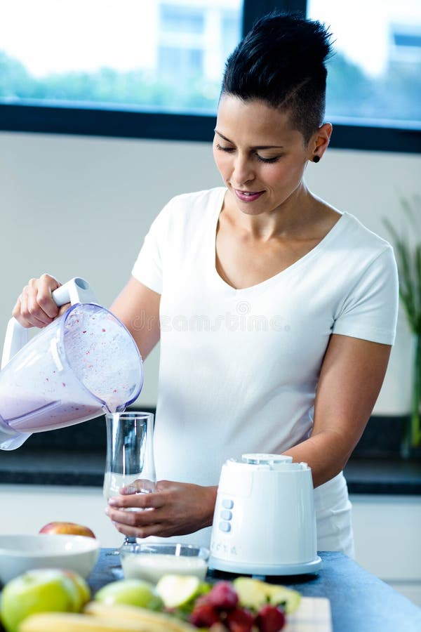 Pregnant woman pouring smoothie in glass in kitchen. Pregnant woman pouring smoothie in glass in kitchen
