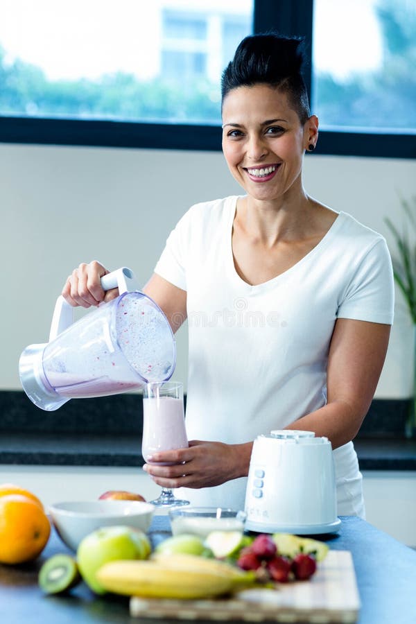 Pregnant woman pouring smoothie in glass in kitchen. Pregnant woman pouring smoothie in glass in kitchen