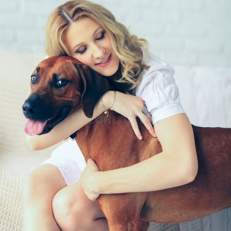 Schwangere Frau und ein Hund, der auf der Couch sitzt. Gl? ckliche schwangere Frau und ein Hund, der auf einer Couchumarmung nett sitzt