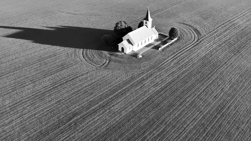 Schwarz-Weiß-Einzelkirche mit einem steilen und langen Schatten in einem riesigen strukturierten Feld. stock footage