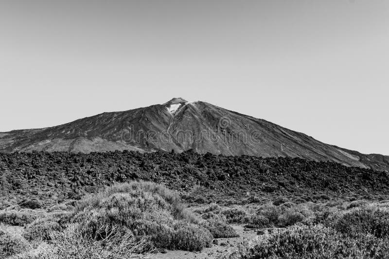 Schwarz-Weiß-Schuss des höchsten Gipfels hinter den Felsen von Arid Lava an einem sonnigen und sehr klaren Tag im Nationalpark El lizenzfreies stockfoto Schwarz-Weiß-Schuss des höchsten Gipfels hinter den Felsen von Arid Lava an einem sonnigen und sehr klaren Tag im Nationalpark El lizenzfreies stockfoto