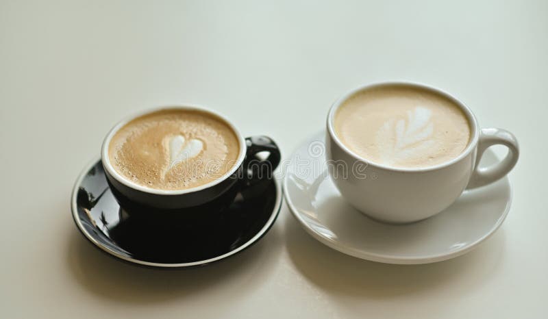 two cups of fresh hot fragrant cappuccino with latte art in the shape of a heart. black and white cups. two cups of fresh hot fragrant cappuccino with latte art in the shape of a heart. black and white cups.