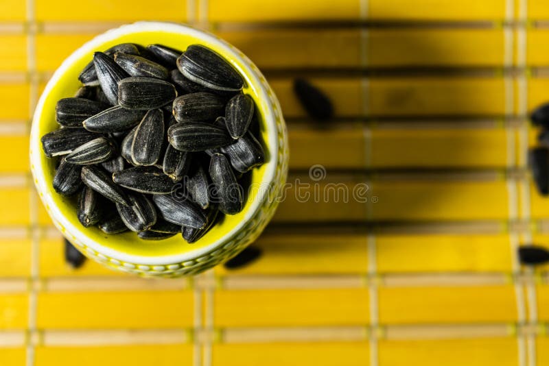 Schwarze kleine Sonnenblumensamen Klicken Sie Samen mit H?lsen an Eine Handvoll in einem gelben Miniaturstand auf einer h?lzernen lizenzfreie stockbilder Schwarze kleine Sonnenblumensamen Klicken Sie Samen mit H?lsen an Eine Handvoll in einem gelben Miniaturstand auf einer h?lzernen lizenzfreie stockbilder