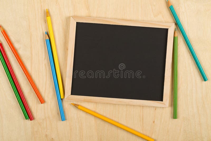 Schwarze, leere, leere Tafel mit farbigen Bleistiften auf dem braunen hölzernen Schreibtisch flach gelegt von oben