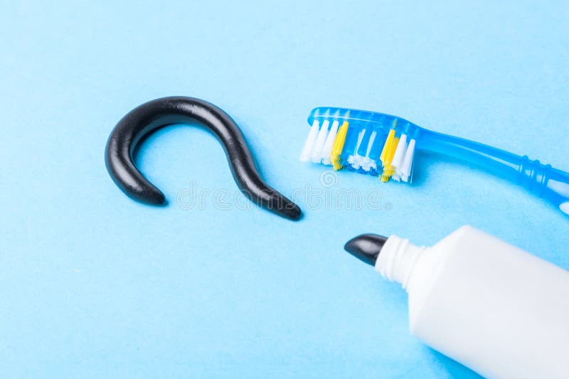 Schwarze Zahnpasta von der Holzkohle für weiße Zähne Zahnpasta in Form von Fragezeichen, Rohr und Zahnbürste auf Blau stockfotografie
