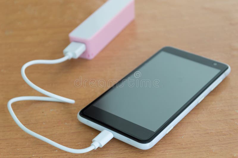 Schwarzer Smartphone mit rosa powerbank auf hölzernem Schreibtisch stockfotografie Schwarzer Smartphone mit rosa powerbank auf hölzernem Schreibtisch stockfotografie