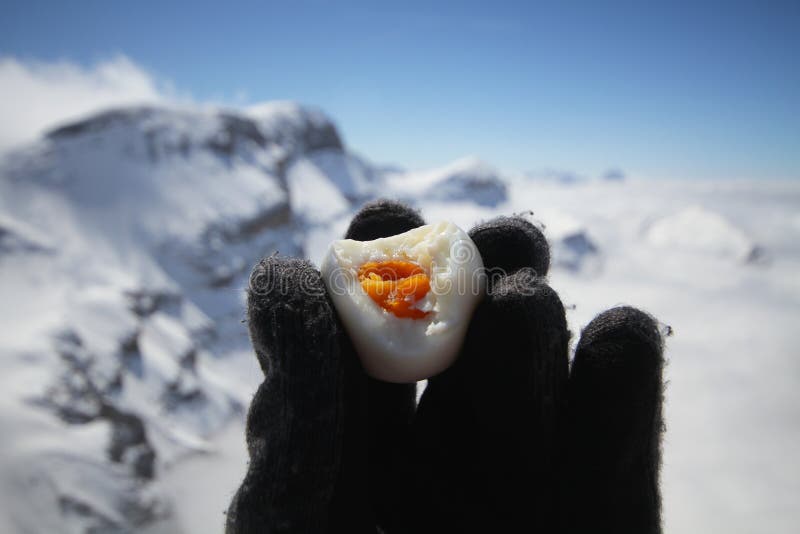 Schwarzer woolen menschlicher Handschuh, der gebissenes heißes frisches gekochtes Ei, Eigelb mitten in Eisgebirgskühlem wetter un stockbilder Schwarzer woolen menschlicher Handschuh, der gebissenes heißes frisches gekochtes Ei, Eigelb mitten in Eisgebirgskühlem wetter un stockbilder