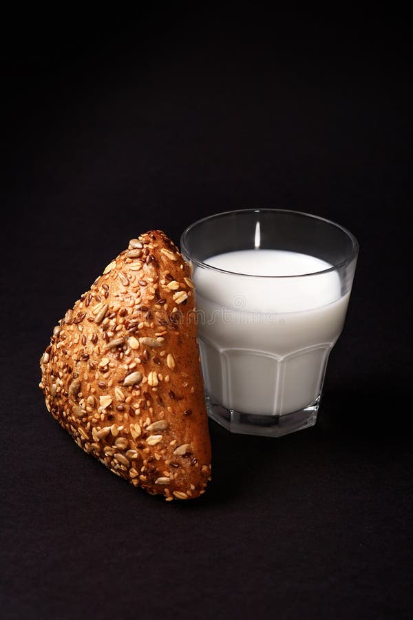 Schwarzes Brötchen mit Samen und Milch Lokalisiert auf Schwarzem lizenzfreies stockbild Schwarzes Brötchen mit Samen und Milch Lokalisiert auf Schwarzem lizenzfreies stockbild