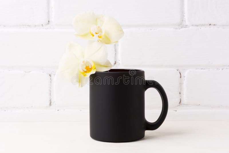 Schwarzes Kaffeetassemodell mit weicher gelber Orchidee lizenzfreie stockbilder Schwarzes Kaffeetassemodell mit weicher gelber Orchidee lizenzfreie stockbilder