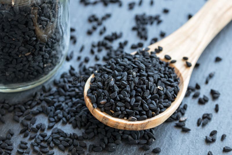 Schwarzkümmelsamen auf einem hölzernen Löffel auf grauem Hintergrund lizenzfreies stockfoto