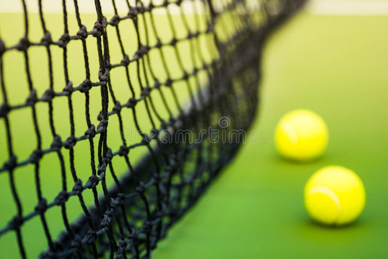 Black weaved net and two tennis balls on green hard court, focus on part of net. Black weaved net and two tennis balls on green hard court, focus on part of net