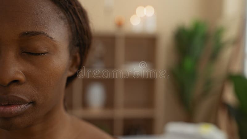 Schöne afrikanische Amerikanerin, die Erholung in einem ruhigen Wellnesscenter mit Kerzen und ruhiger Atmosphäre genießt stockfotografie