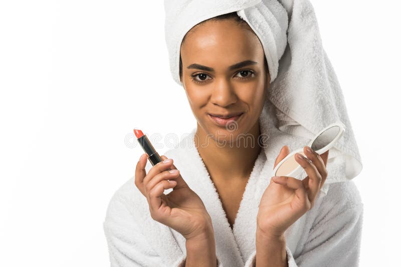 schöne Afroamerikanerfrau im Bademantel und in Tuch, die Lippenstift und Spiegel halten, lizenzfreies stockbild schöne Afroamerikanerfrau im Bademantel und in Tuch, die Lippenstift und Spiegel halten, lizenzfreies stockbild