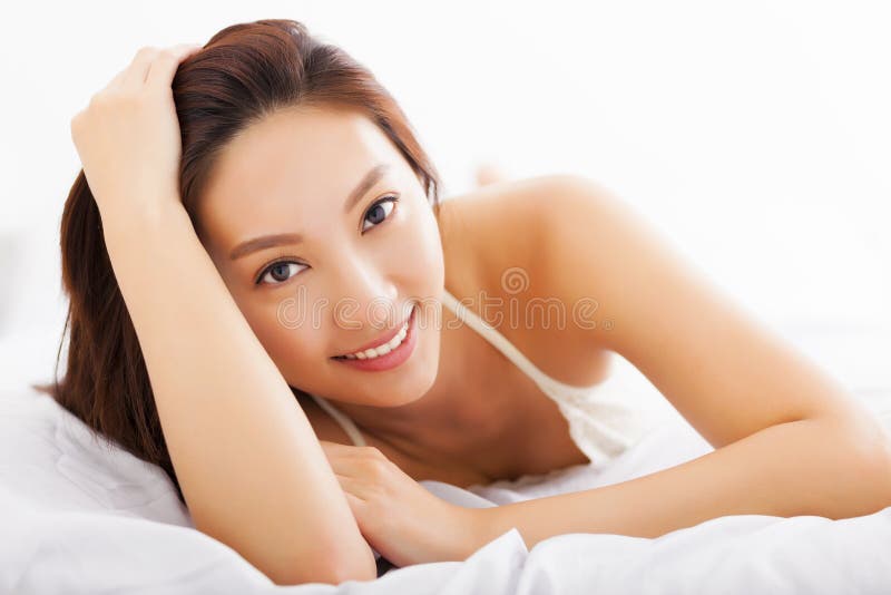 Schöne asiatische Frau, die auf dem Bett sich entspannt stockbild