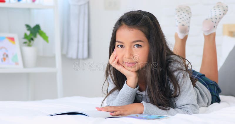 Schöne asiatische junge Brunettefrau, die zu Hause ein Buch auf dem Bett mit Lächelngesicht liest
