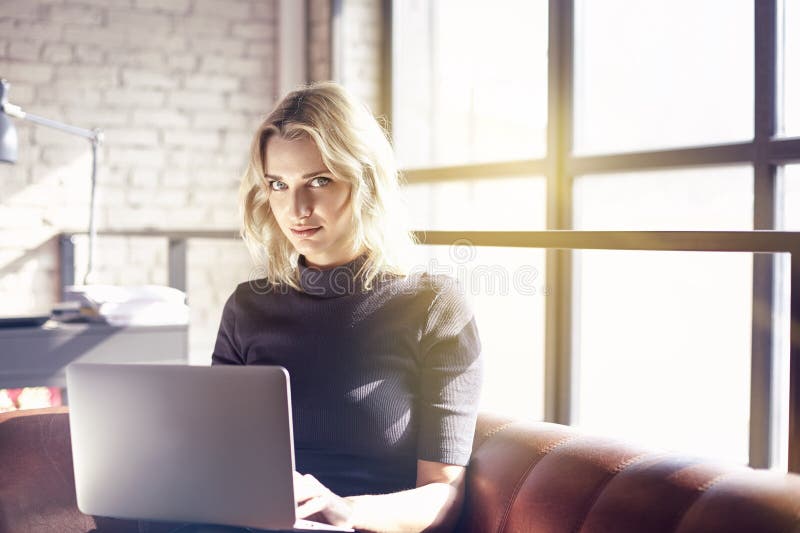 Schöne blonde Geschäftsfrau, die im sonnigen Büro arbeitet auf Laptop sitzt Konzept von Arbeitstragbaren geräten der jungen Leute lizenzfreie stockfotos Schöne blonde Geschäftsfrau, die im sonnigen Büro arbeitet auf Laptop sitzt Konzept von Arbeitstragbaren geräten der jungen Leute lizenzfreie stockfotos