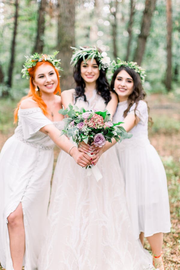 Schöne Braut in stilvollem rustikalem Kleid und Kranz hält Blumenstrauß in ihren Händen Zwei schöne Jungfernhäuser stockfoto