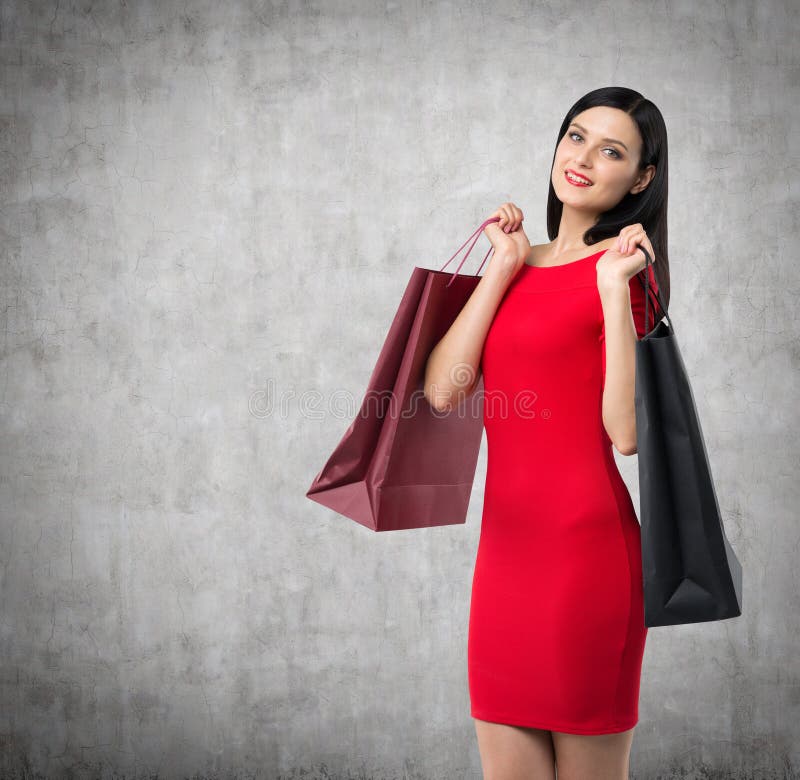 Schöne Brunettefrau in einem roten Kleid hält fantastische Einkaufstaschen lizenzfreie stockfotos Schöne Brunettefrau in einem roten Kleid hält fantastische Einkaufstaschen lizenzfreie stockfotos