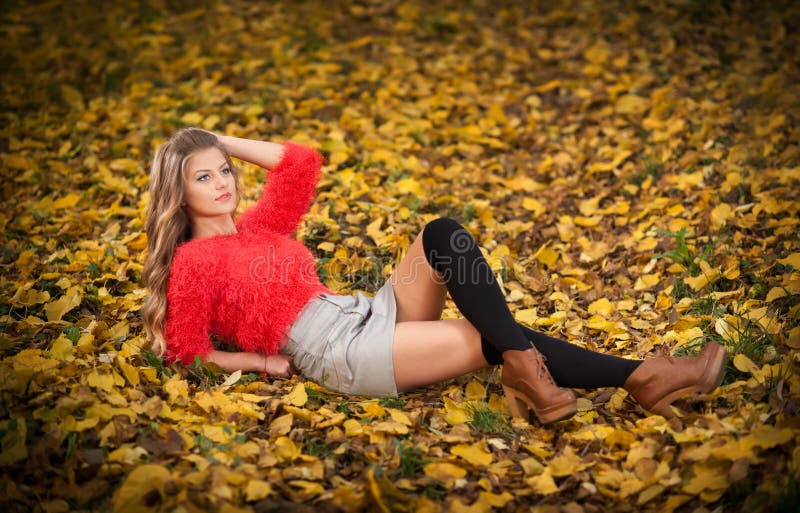 Beautiful elegant woman with red blouse and short skirt posing in park during fall. Young pretty woman with blonde hair lying down on autumnal leaves. Sensual blonde with black leggings in forest. Beautiful elegant woman with red blouse and short skirt posing in park during fall. Young pretty woman with blonde hair lying down on autumnal leaves. Sensual blonde with black leggings in forest.