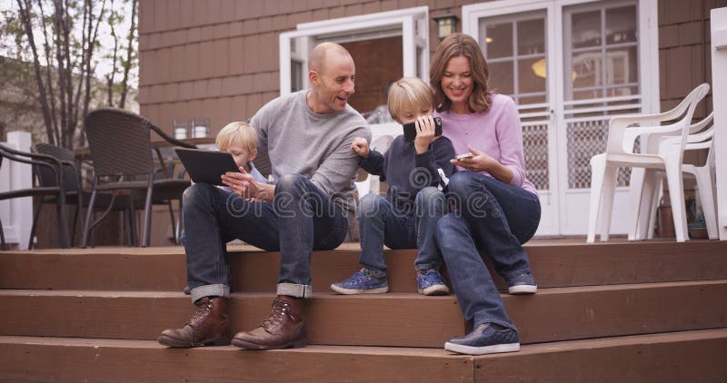 Schöne Familie, die draußen Handgeräte betrachtet lizenzfreies stockbild