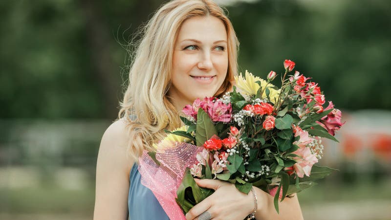 Schöne Frau mit Blumenstrauß auf dem Gras im Stadtpark stockbilder
