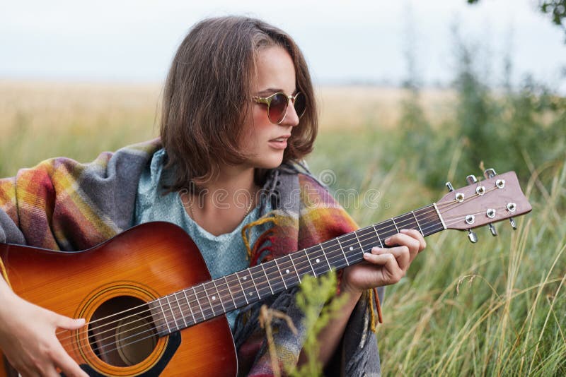 Schöne Frau mit der Kurzhaarfrisur, welche die stilvolle Sonnenbrille stillsteht Gitarre trägt draußen, spielend ihre Sommerferie stockfoto Schöne Frau mit der Kurzhaarfrisur, welche die stilvolle Sonnenbrille stillsteht Gitarre trägt draußen, spielend ihre Sommerferie stockfoto