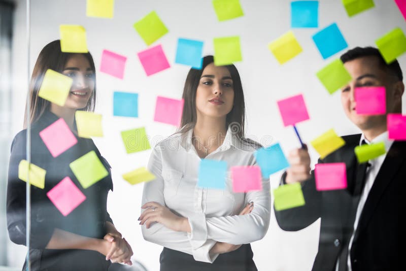 Schöne Geschäftsleute benutzen Aufkleber und Markierung, besprechen Ideen und lächeln während der Konferenz im Büro Team Arbeit stockbild Schöne Geschäftsleute benutzen Aufkleber und Markierung, besprechen Ideen und lächeln während der Konferenz im Büro Team Arbeit stockbild