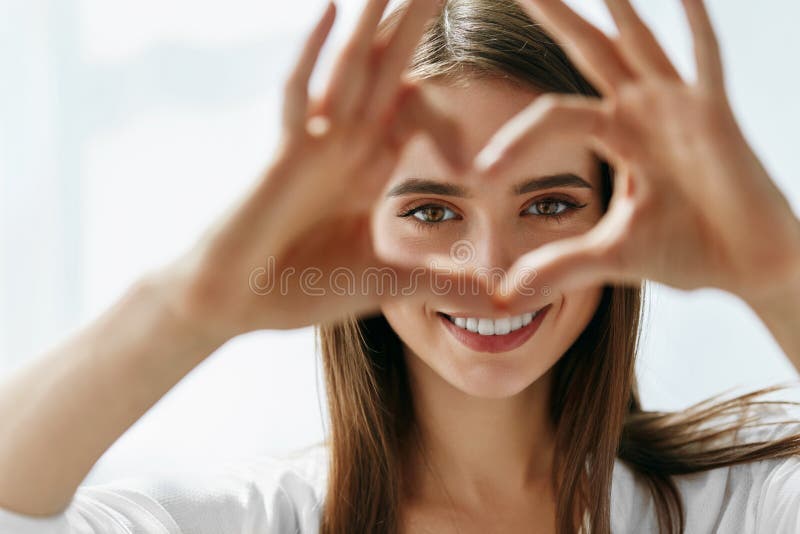 Schöne glückliche Frau, die Liebes-Zeichen nahe Augen zeigt stockbild