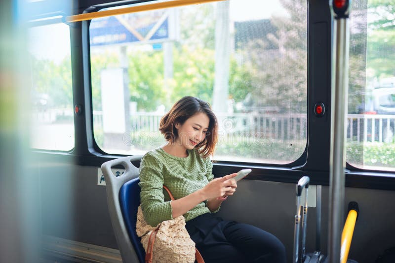 Schöne glückliche junge Frau, die im Stadtbus sitzt und das Handy anschaut stockbilder