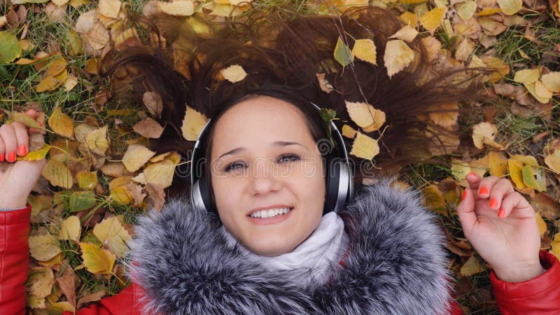 Schöne glückliche junge Frau mit den Kopfhörern, die auf Herbstlaub hörend Musik liegen Jahreszeit, Technologie und Leute lizenzfreie stockbilder Schöne glückliche junge Frau mit den Kopfhörern, die auf Herbstlaub hörend Musik liegen Jahreszeit, Technologie und Leute lizenzfreie stockbilder