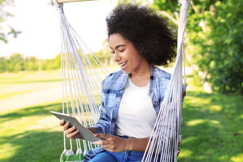 Schöne junge afro-amerikanische Frau mit dem Tablet-Computer, der draußen in der Hängematte stillsteht stockbild Schöne junge afro-amerikanische Frau mit dem Tablet-Computer, der draußen in der Hängematte stillsteht stockbild