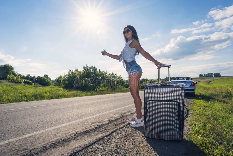 Schöne junge Dame auf Landstraße mit Koffer per Anhalter fahrend auf sonniger Tages-Freienlandschaft-backround Frau ausgedehnt lizenzfreie stockfotos Schöne junge Dame auf Landstraße mit Koffer per Anhalter fahrend auf sonniger Tages-Freienlandschaft-backround Frau ausgedehnt lizenzfreie stockfotos