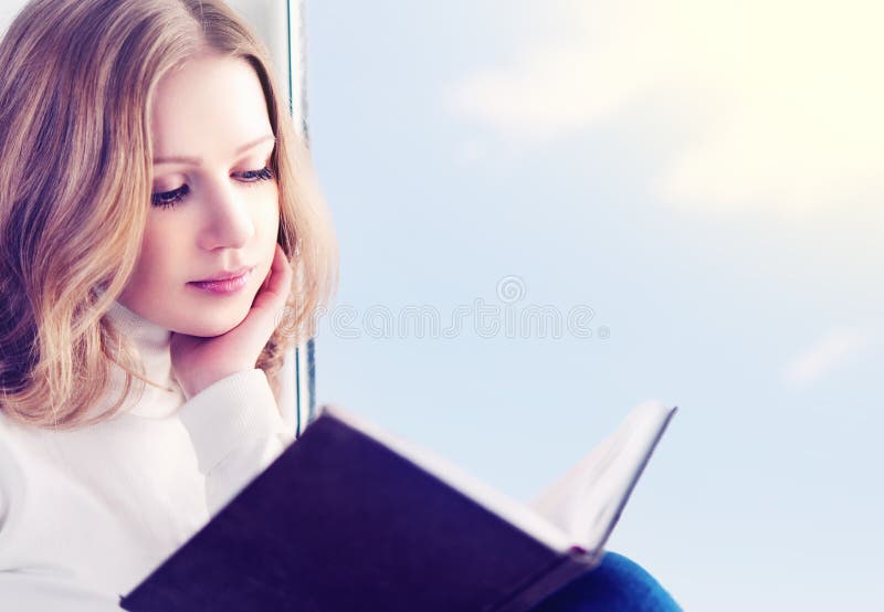 Schöne junge Frau, die ein Buch beim Sitzen an einem Fenster liest lizenzfreie stockbilder Schöne junge Frau, die ein Buch beim Sitzen an einem Fenster liest lizenzfreie stockbilder