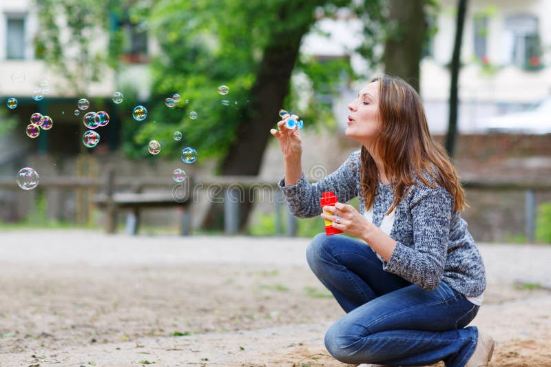 Schöne junge Frau, die mit Seifenblasen im Park spielt stockfotografie Schöne junge Frau, die mit Seifenblasen im Park spielt stockfotografie