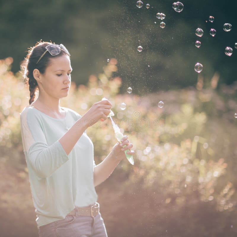 Schöne junge Frau, die mit Seifenblasen in Sunny Park spielt lizenzfreies stockbild Schöne junge Frau, die mit Seifenblasen in Sunny Park spielt lizenzfreies stockbild