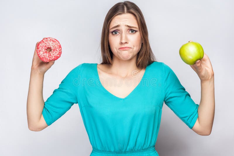 Schöne junge Frau mit den Sommersprossen im grünen Kleid, confussed und versuchend, Wahl zwischen Apfel und Donut zu treffen lizenzfreie stockfotos Schöne junge Frau mit den Sommersprossen im grünen Kleid, confussed und versuchend, Wahl zwischen Apfel und Donut zu treffen lizenzfreie stockfotos