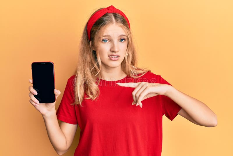 Beautiful young caucasian girl holding smartphone showing screen clueless and confused expression. doubt concept. Beautiful young caucasian girl holding smartphone showing screen clueless and confused expression. doubt concept