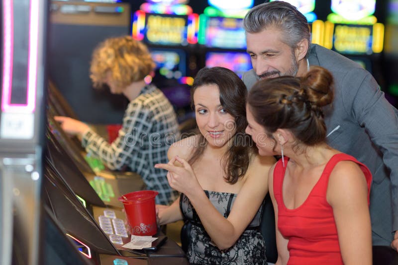 Schöne junge Leute nähern sich Spielautomaten im Kasino lizenzfreie stockfotografie Schöne junge Leute nähern sich Spielautomaten im Kasino lizenzfreie stockfotografie