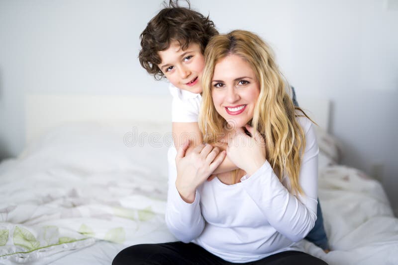 Schöne junge Mutter und Sohn, die zusammen auf einem Bett liegt