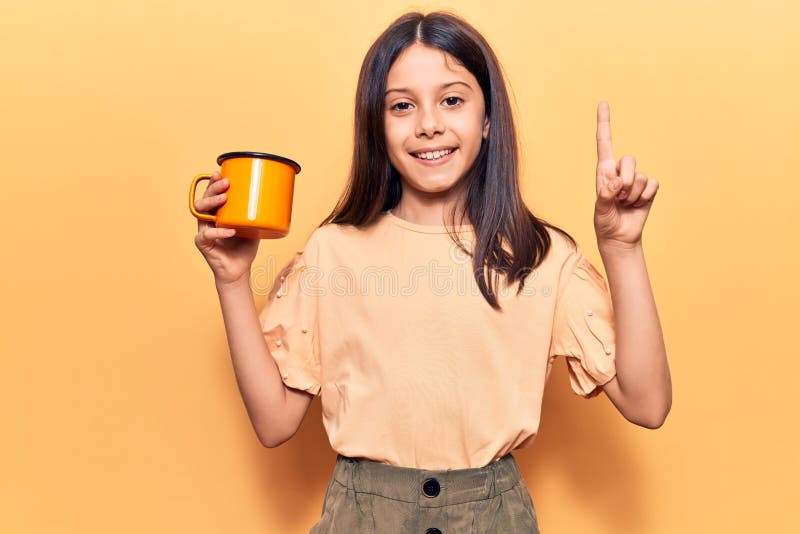 Schöne Kind Mädchen halten Kaffee lächelnd mit einer Idee oder Frage Zeigefinger mit glücklichen Gesicht Nummer eins lizenzfreies stockbild