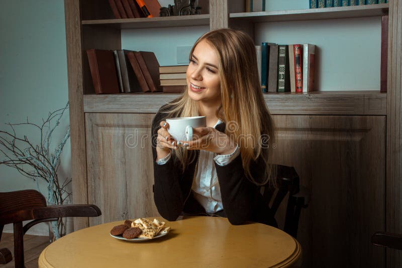 Schöne lächelnde Frau an einem Tisch mit einer Schale in seinen Händen stockbild Schöne lächelnde Frau an einem Tisch mit einer Schale in seinen Händen stockbild