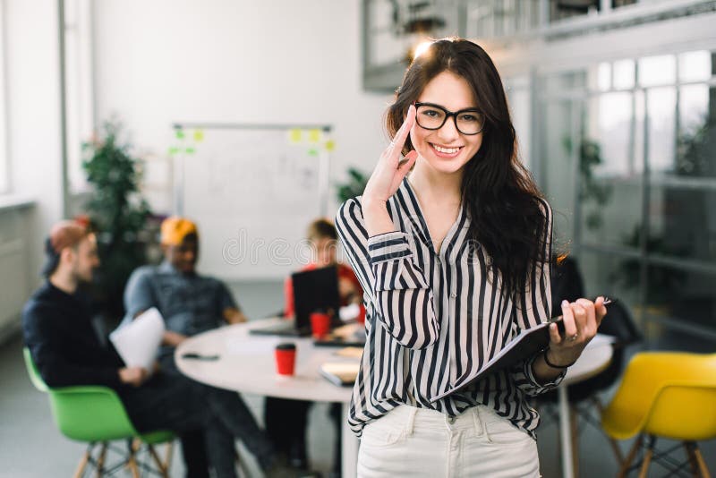 Schöne modische brunette Geschäftsfrau in den Gläsern mit Ordner von Dokumenten in ihren Händen zuhause Team von jungen Arbeitneh stockfoto Schöne modische brunette Geschäftsfrau in den Gläsern mit Ordner von Dokumenten in ihren Händen zuhause Team von jungen Arbeitneh stockfoto