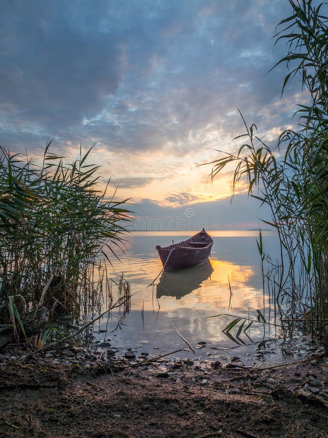 Schöne Morgenlandschaft mit einem Boot auf dem See bei dem Sonnenaufgang durch das Schilf lizenzfreies stockbild Schöne Morgenlandschaft mit einem Boot auf dem See bei dem Sonnenaufgang durch das Schilf lizenzfreies stockbild